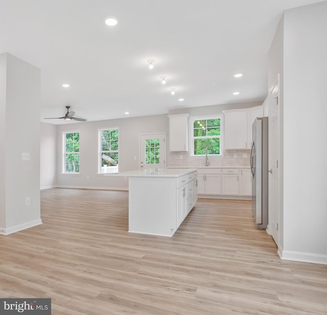 kitchen with light hardwood / wood-style flooring, stainless steel fridge, ceiling fan, decorative backsplash, and white cabinets