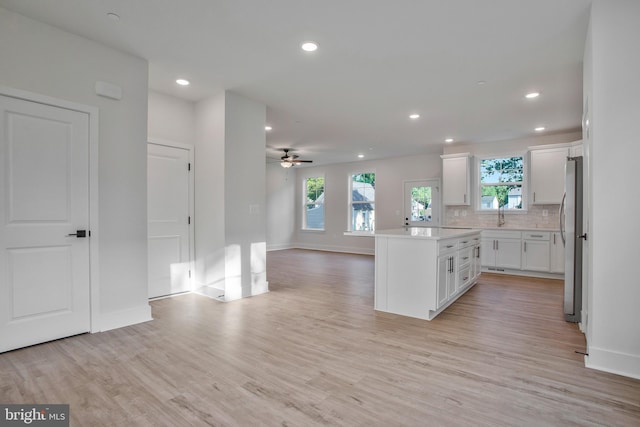 kitchen with white cabinetry, a center island, light hardwood / wood-style flooring, stainless steel fridge, and backsplash