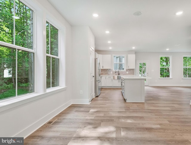 kitchen featuring stainless steel refrigerator, white cabinetry, backsplash, a center island, and light hardwood / wood-style flooring