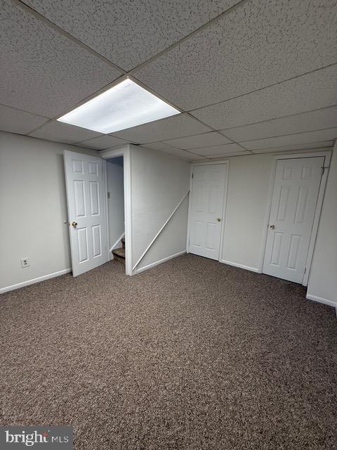 basement with a paneled ceiling and dark colored carpet