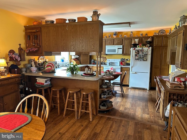 kitchen featuring dark wood-type flooring, kitchen peninsula, white appliances, and a breakfast bar area