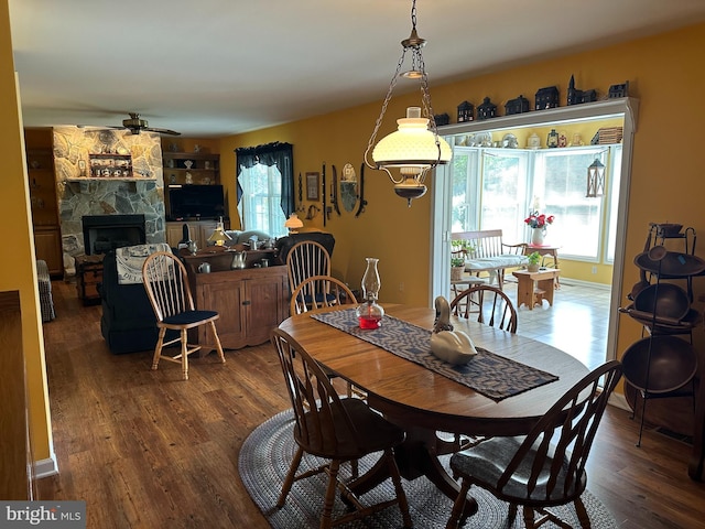 dining space with a stone fireplace, dark hardwood / wood-style floors, and ceiling fan