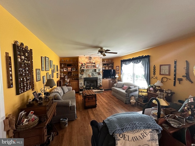 living room featuring built in features, wood-type flooring, a fireplace, and ceiling fan