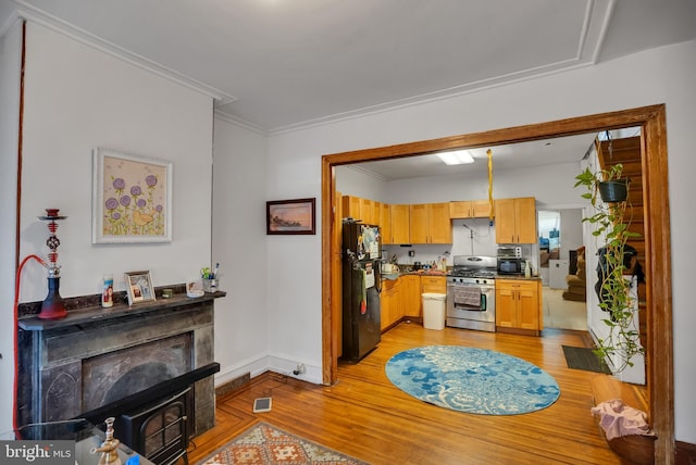 kitchen featuring black refrigerator, ornamental molding, light hardwood / wood-style floors, gas stove, and light brown cabinets