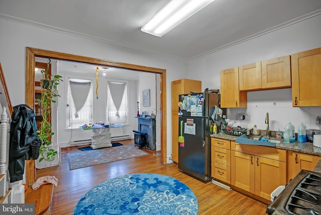 kitchen featuring sink, crown molding, light hardwood / wood-style flooring, black refrigerator, and light stone counters