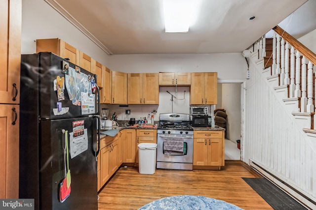 kitchen featuring light brown cabinetry, dark stone counters, baseboard heating, black fridge, and stainless steel range with gas stovetop