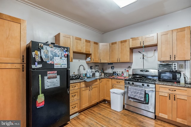 kitchen featuring sink, dark stone counters, black appliances, light brown cabinets, and light hardwood / wood-style flooring