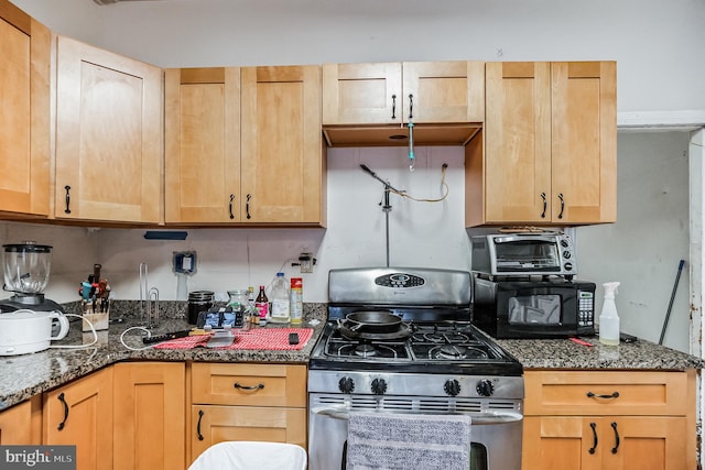 kitchen featuring dark stone countertops, gas stove, and light brown cabinets