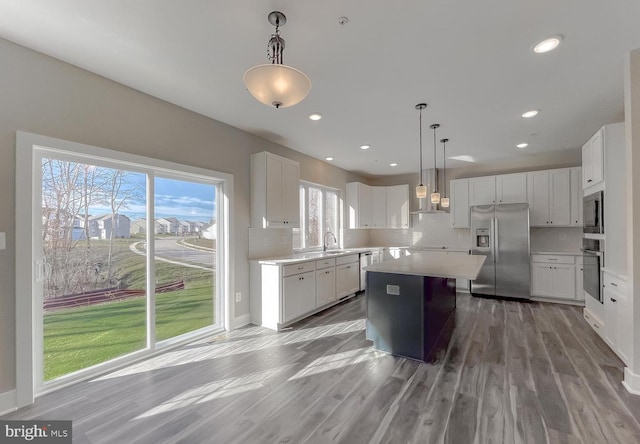 kitchen featuring white cabinetry, decorative light fixtures, a center island, and appliances with stainless steel finishes