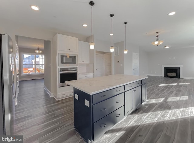 kitchen with white cabinetry, a center island, pendant lighting, stainless steel appliances, and light stone countertops