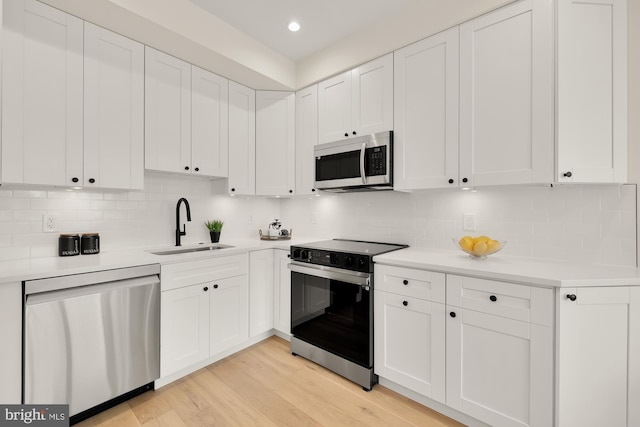 kitchen with light hardwood / wood-style floors, appliances with stainless steel finishes, white cabinets, and decorative backsplash