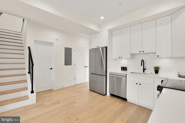 kitchen with light hardwood / wood-style flooring, stainless steel appliances, sink, backsplash, and white cabinetry