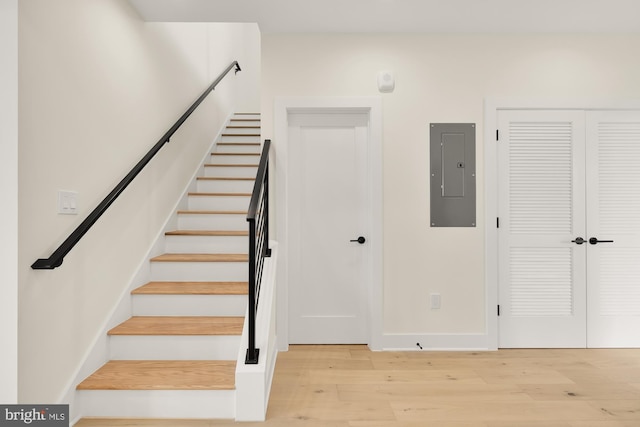 stairway with light hardwood / wood-style flooring and electric panel