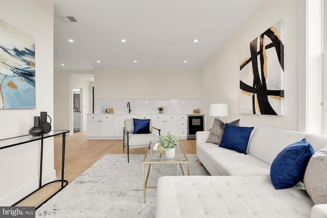 living room with beverage cooler, light hardwood / wood-style floors, and sink