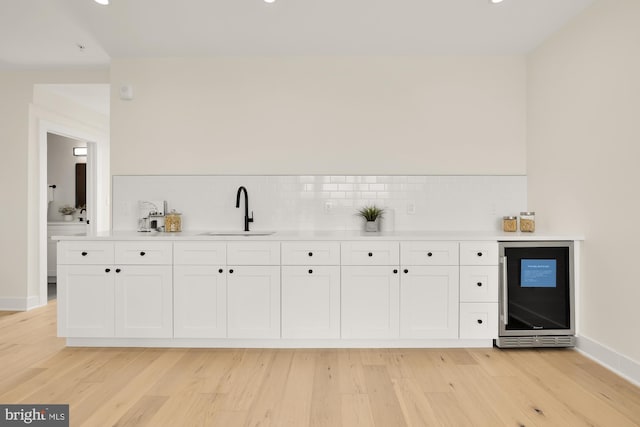 bar with white cabinetry, light hardwood / wood-style flooring, tasteful backsplash, and sink