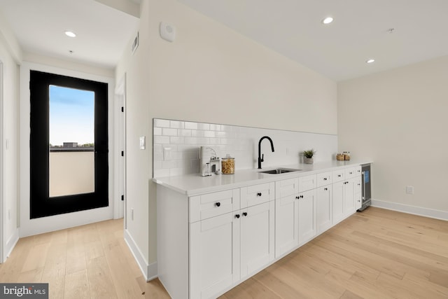 kitchen featuring white cabinetry, tasteful backsplash, beverage cooler, light hardwood / wood-style floors, and sink