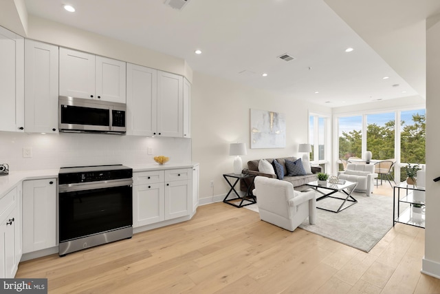 kitchen featuring decorative backsplash, appliances with stainless steel finishes, white cabinets, and light hardwood / wood-style floors