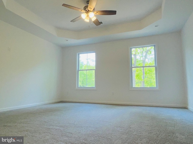 spare room with ceiling fan, a raised ceiling, and light carpet