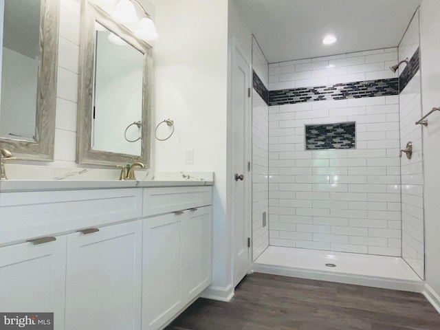 bathroom with hardwood / wood-style flooring, tiled shower, and vanity