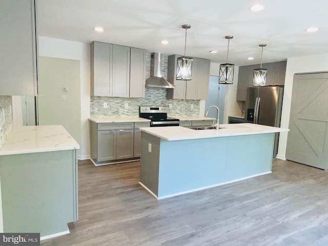 kitchen with hanging light fixtures, appliances with stainless steel finishes, a barn door, hardwood / wood-style floors, and wall chimney range hood