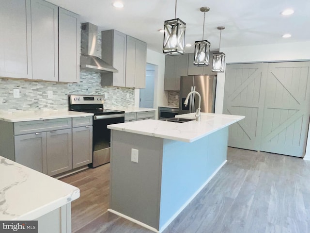 kitchen featuring hardwood / wood-style flooring, a kitchen island with sink, stainless steel appliances, light stone counters, and wall chimney exhaust hood