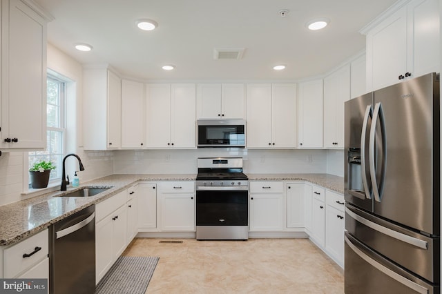 kitchen featuring backsplash, light stone counters, stainless steel appliances, white cabinetry, and a sink