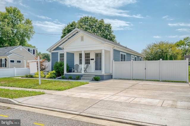 view of front of property featuring a front lawn, fence, covered porch, driveway, and a gate