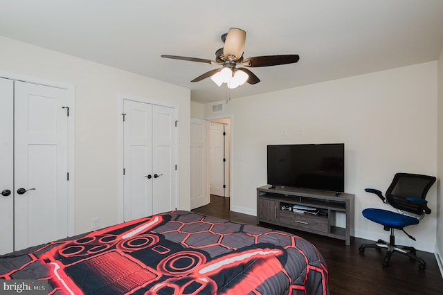 bedroom with dark wood-type flooring, ceiling fan, and multiple closets