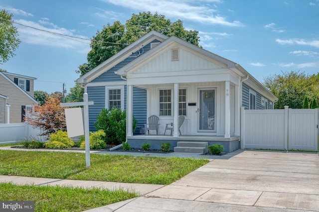 view of front of home with board and batten siding, covered porch, a front lawn, and fence