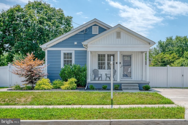 bungalow-style house featuring board and batten siding, covered porch, a front lawn, and fence