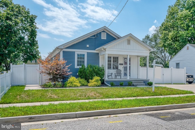 bungalow-style house with a gate, fence, covered porch, a front lawn, and board and batten siding