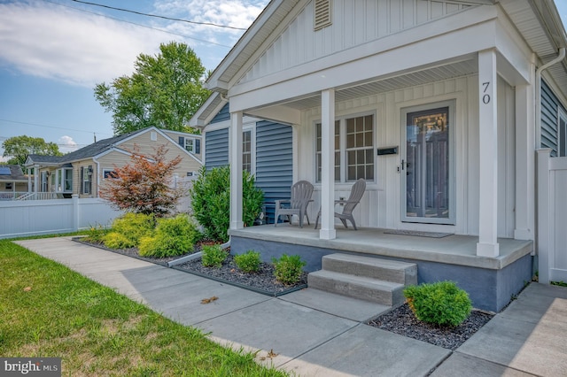 property entrance with board and batten siding, a porch, and fence