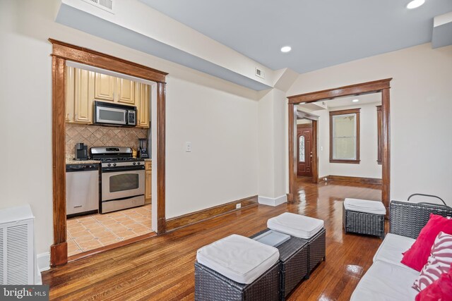 kitchen featuring appliances with stainless steel finishes, cream cabinetry, hardwood / wood-style flooring, and backsplash