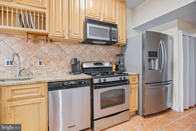 kitchen featuring light stone counters, appliances with stainless steel finishes, light tile patterned flooring, tasteful backsplash, and sink