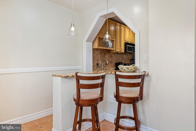 bar featuring light tile patterned flooring, hanging light fixtures, light stone countertops, backsplash, and sink