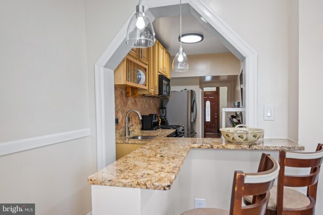 kitchen with stainless steel refrigerator, hanging light fixtures, range, backsplash, and sink