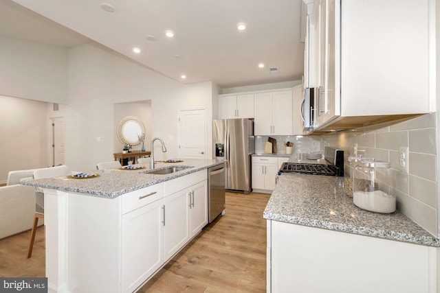 kitchen featuring an island with sink, light wood-type flooring, sink, light stone counters, and appliances with stainless steel finishes