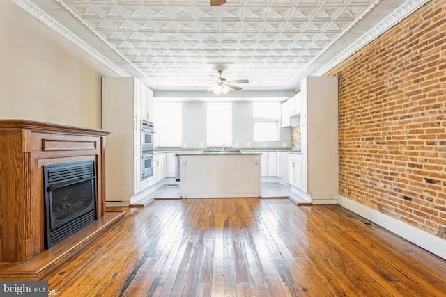 unfurnished living room featuring ceiling fan, sink, brick wall, and wood-type flooring