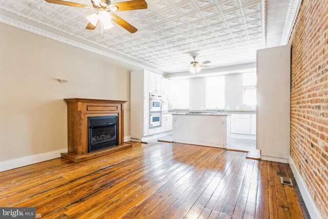 unfurnished living room with brick wall, ceiling fan, and light hardwood / wood-style flooring