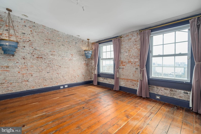 empty room featuring hardwood / wood-style flooring and brick wall