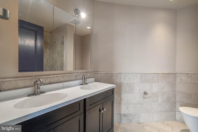 bathroom with tiled shower, vanity, tile walls, and toilet