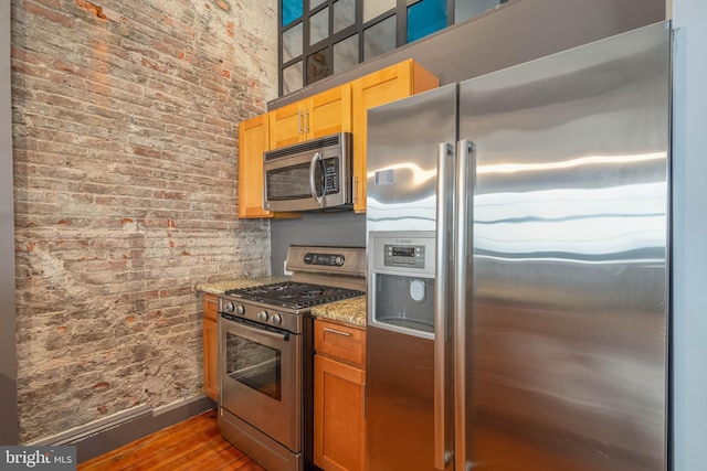 kitchen with light stone countertops, stainless steel appliances, brick wall, and dark wood-type flooring