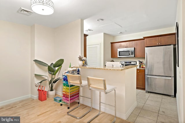 kitchen with stainless steel appliances, light stone countertops, a breakfast bar, light hardwood / wood-style flooring, and kitchen peninsula