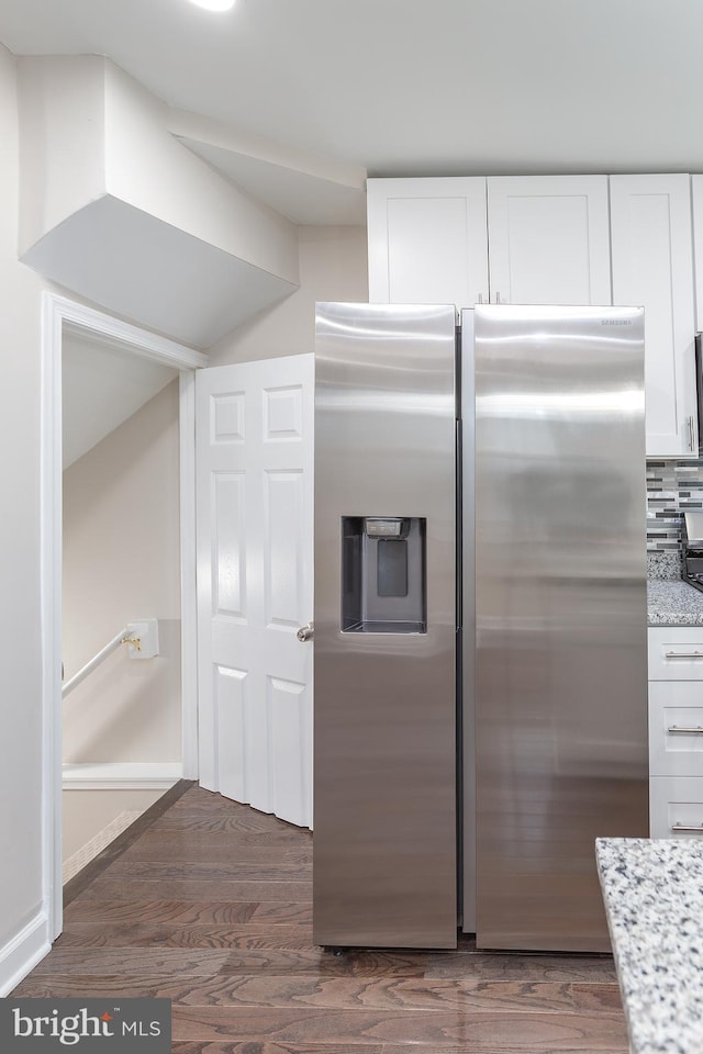 kitchen with white cabinetry, backsplash, stainless steel fridge, light stone counters, and dark wood-type flooring