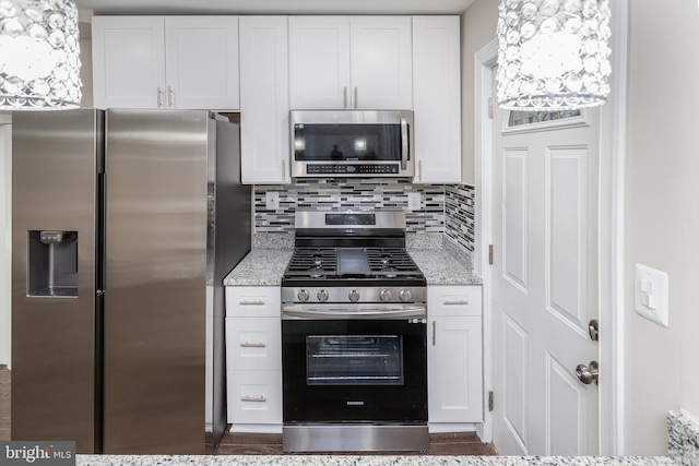 kitchen with tasteful backsplash, appliances with stainless steel finishes, white cabinets, and light stone counters