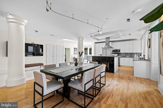 dining room featuring light wood-type flooring, decorative columns, and sink