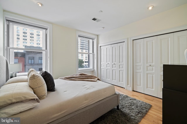 bedroom featuring light hardwood / wood-style flooring, multiple windows, and two closets