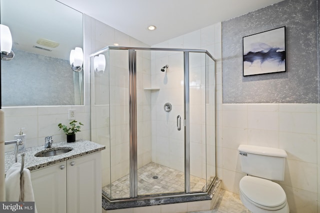 bathroom with tile walls, a shower with door, vanity, and toilet