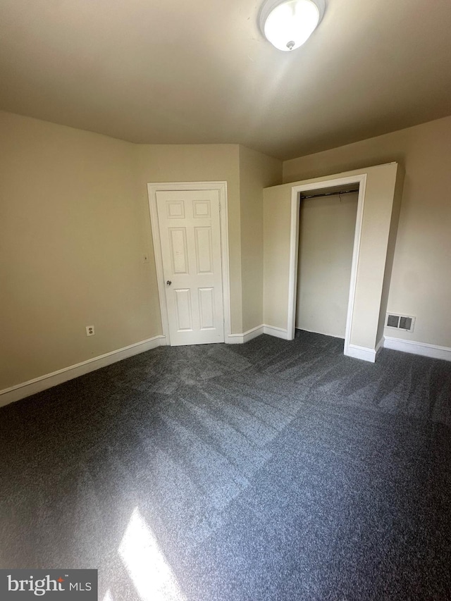 unfurnished bedroom with dark colored carpet and a closet