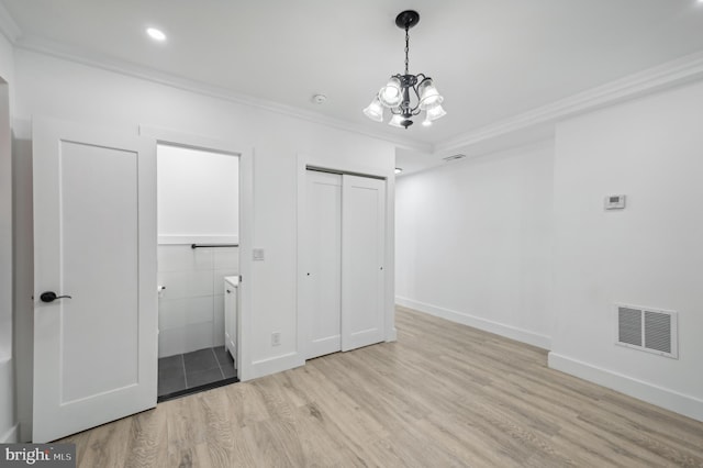 unfurnished bedroom featuring connected bathroom, ornamental molding, light hardwood / wood-style floors, an inviting chandelier, and a closet